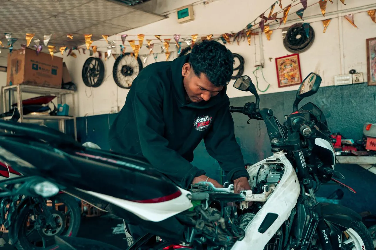 Mechanic in a Rev and Ride hoodie servicing a white Pulsar